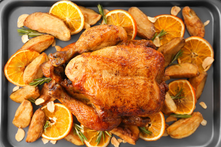 Roasted turkey with slices of orange and potatoes on baking sheetの写真素材