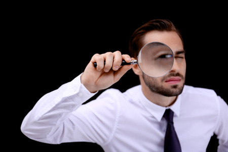 Handsome young man with magnifier on dark backgroundの写真素材
