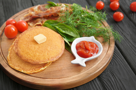 Tasty breakfast with pancakes, bacon and vegetables on wooden boardの写真素材