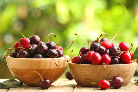 Wooden bowls with fresh cherry on table outdoorsの写真素材