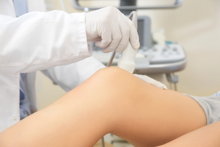 Doctor conducting ultrasound examination of woman's knee in clinicの写真素材