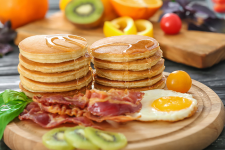 Tasty breakfast with pancakes, fried egg and bacon on wooden boardの写真素材