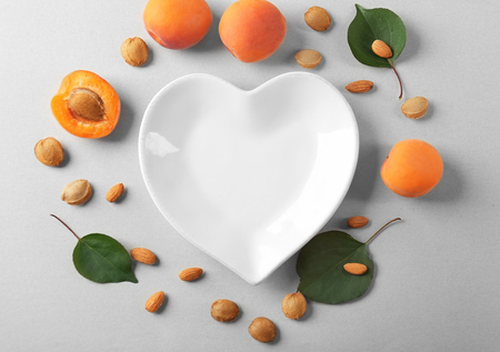 Composition of apricots with kernels and plate in shape of heart on light backgroundの写真素材
