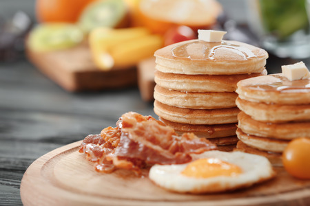 Tasty breakfast with pancakes, fried egg and bacon on wooden boardの写真素材