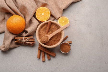 Cinnamon sticks and sugar in wooden bowl with oranges on grey backgroundの写真素材