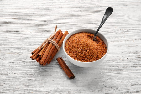 White bowl with cinnamon sugar and sticks on wooden backgroundの写真素材