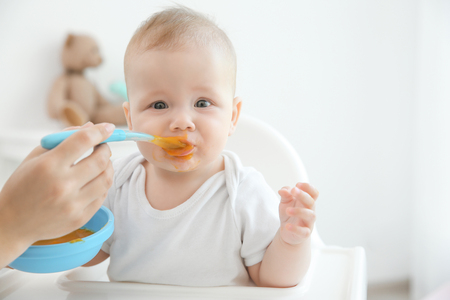 Mother feeding baby with spoon indoorsの写真素材