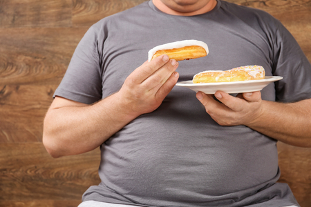 Overweight young man eating sweets on wooden backgroundの写真素材