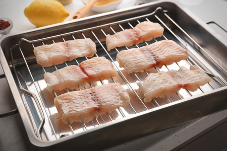 Raw slices of fish fillet on roasting pan in kitchenの写真素材