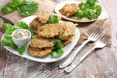 Delicious broccoli pancakes served with sauce and fresh basil leaves on wooden backgroundの写真素材