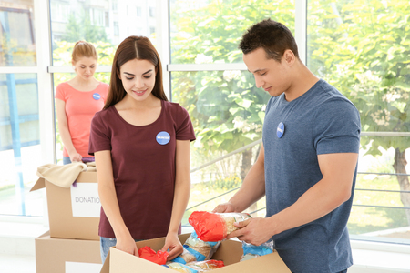 Teen volunteers collecting donated food in cardboard box indoorsの写真素材