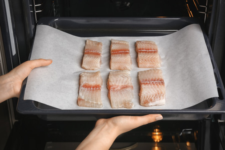 Woman putting baking tray with fish fillet slices in ovenの写真素材