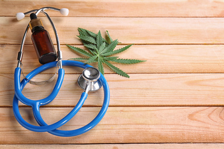 Stethoscope with hemp leaves and bottle of oil on wooden background. Alternative medicine conceptの写真素材
