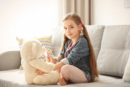 Adorable little girl examining teddy bear with stethoscope at homeの写真素材