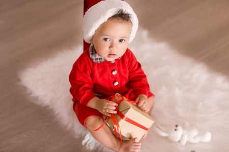 Cute little baby in Santa hat with gift box sitting on floorの写真素材