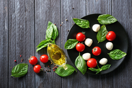 Composition with mozzarella cheese balls, cherry tomatoes and green fresh organic basil on wooden backgroundの写真素材