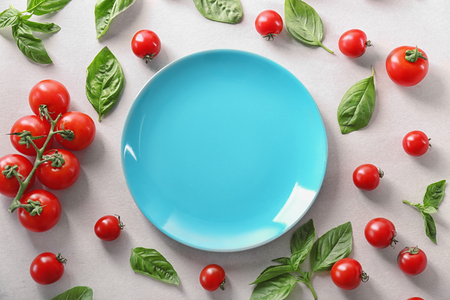 Composition with blue plate, cherry tomatoes and green fresh organic basil on light backgroundの写真素材