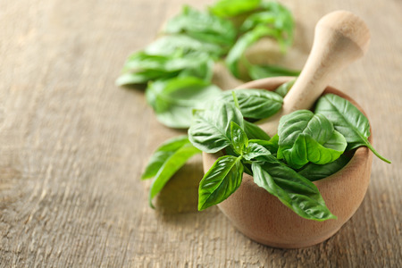 Green fresh organic basil leaves in wooden mortar on wooden backgroundの写真素材