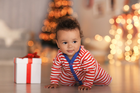 Cute little baby with gift box on floor and blurred Christmas lights on backgroundの写真素材