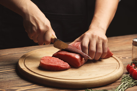 Chef cutting fresh raw meat on wooden boardの写真素材