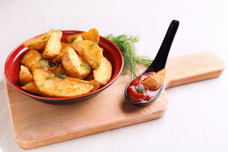 Bowl with delicious baked potato wedges on wooden boardの写真素材