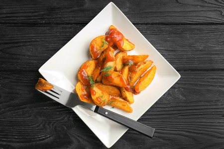 Plate with delicious baked potato wedges and sauce on wooden background