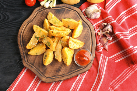 Wooden board with delicious baked potato wedges and sauce on tableの写真素材