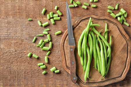 Wooden board and fresh green beans on table