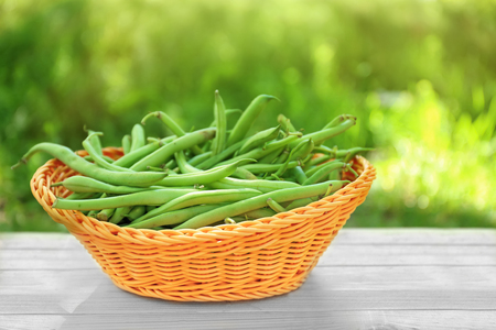 Wicker basket with raw fresh organic green beans on table outdoorsの写真素材