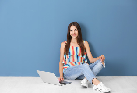 Young woman sitting with laptop near color wall