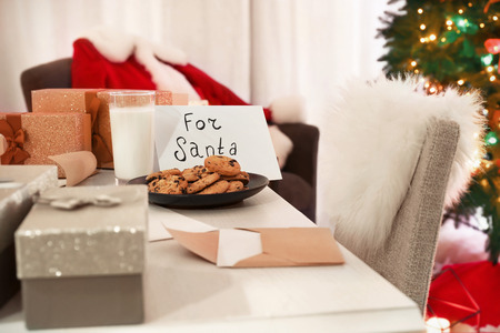 Table with cookies and glass of milk for Santa in room decorated for Christmasの写真素材