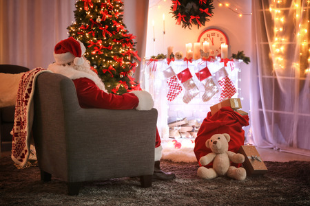 Authentic Santa Claus sitting in armchair at room decorated for Christmasの写真素材