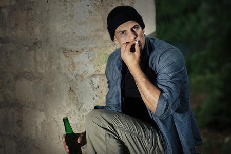 Man sitting with cigarette and bottle of alcohol in abandoned buildingの写真素材
