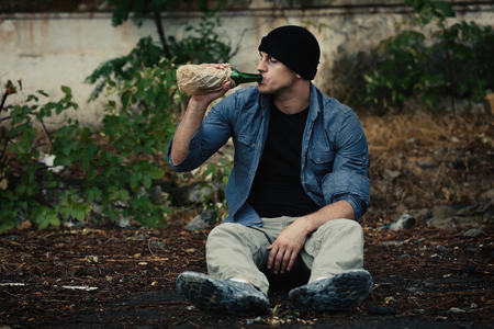 Man sitting on ground and drinking alcohol outdoorsの写真素材