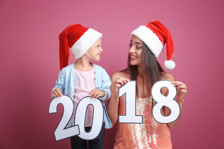 Young woman and cute little girl in Santa hats with paper figures 2018 on color background. Christmas celebration conceptの写真素材