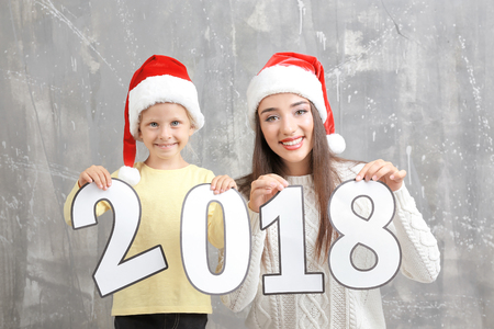 Young woman and cute little girl with paper figures 2018 on grunge background. Christmas celebration conceptの写真素材