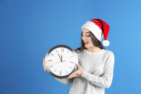 Young woman in Santa hat with clock on color background. Christmas countdown concept