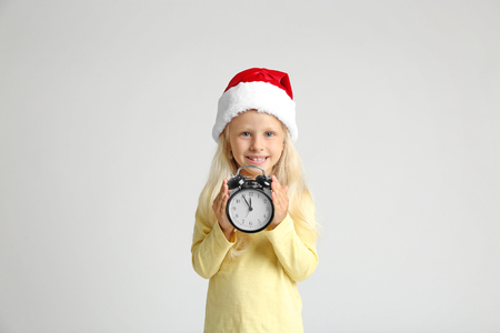 Cute little girl in Santa hat with clock on light background. Christmas countdown conceptの写真素材