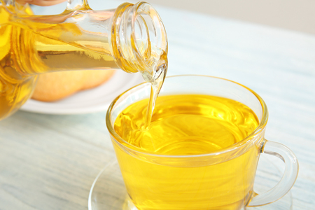 Pouring oil into glass cup on wooden  backgroundの写真素材
