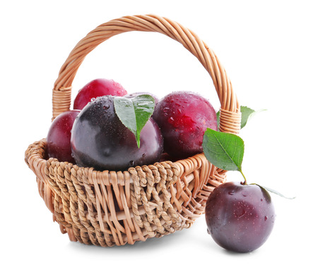 Wicker basket with fresh ripe plums on white backgroundの写真素材