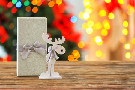 Christmas gift box and decorative deer on wooden table against blurred backgroundの写真素材