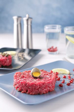 Delicious steak tartare with yolk in egg shell and pomegranate seeds on plateの写真素材