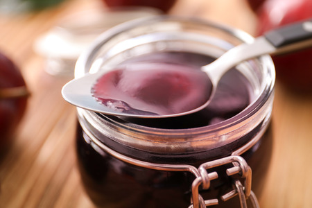 Spoon and jar with tasty plum jam on tableの写真素材