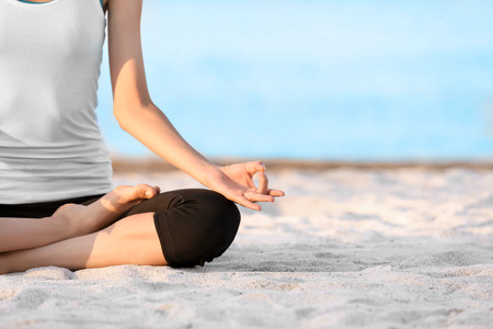 Beautiful young woman practicing yoga on sea beachの写真素材