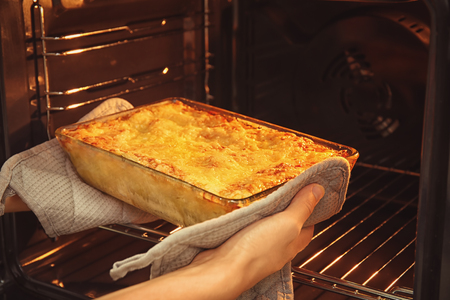 Woman taking baking tray with spinach lasagna out of ovenの写真素材