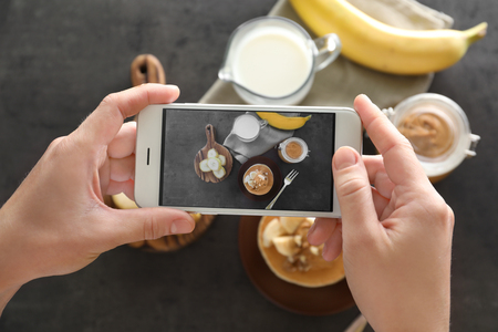 Woman taking photo of delicious food with mobile phoneの写真素材