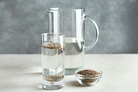 Glass of water and bowl with chia seeds on tableの写真素材