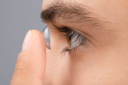 Young man putting contact lens in his eye on grey background, closeupの写真素材