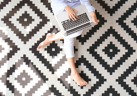 Young woman using laptop while sitting on carpetの写真素材