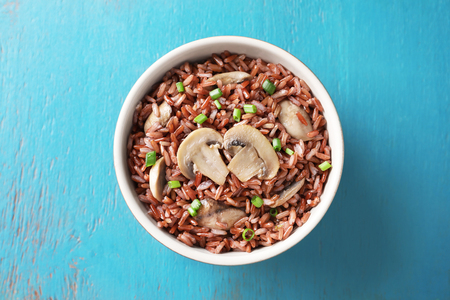 Bowl with tasty brown rice and mushrooms on color wooden backgroundの写真素材